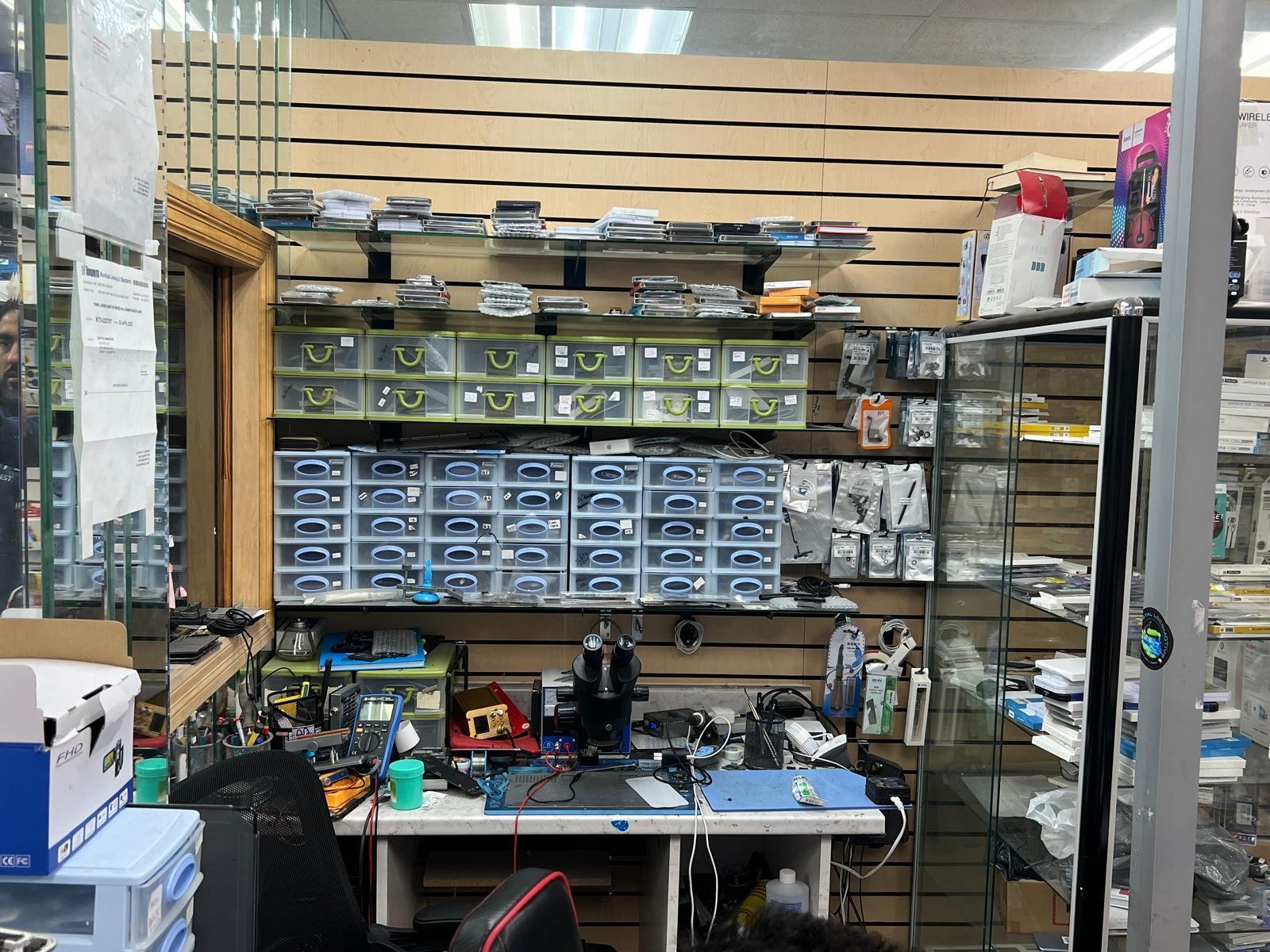 An electronics workshop with shelves and drawers neatly organized with small parts, tools, and electronic components. A workbench in the foreground has a microscope and other repair equipment. Location: Toronto, Canada