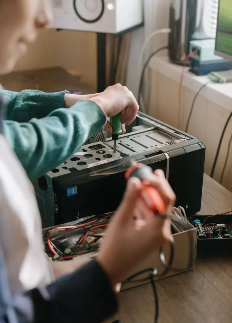 A child is seen from the chest up, focused on assembling or disassembling a computer tower with a screwdriver. Wires and electronic components are visible in a box in the foreground. Location: Toronto, Canada