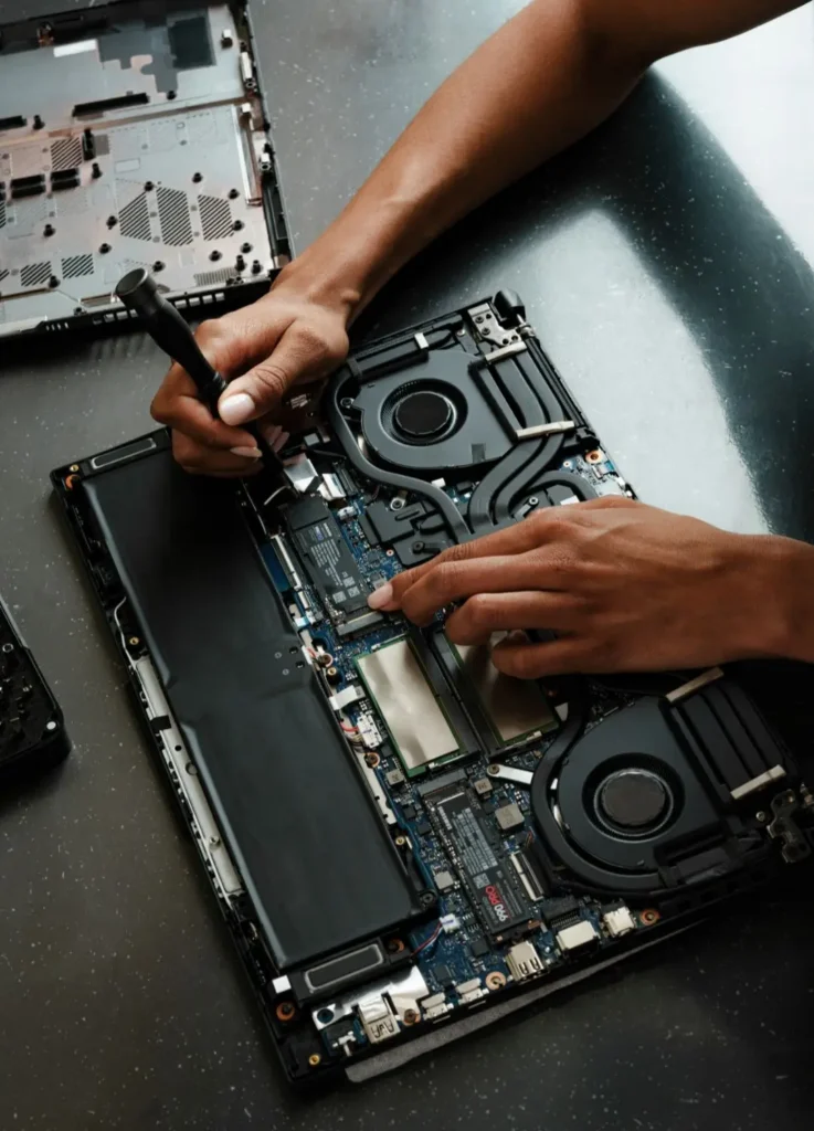 A person's hands are shown working on the internal components of a disassembled laptop. One hand holds a screwdriver, while the other points to the motherboard. Location: Toronto, Canada